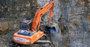 Bagger mit Erdbau-Hake-Beschriftung löst Kalkstein an der Abbauwand