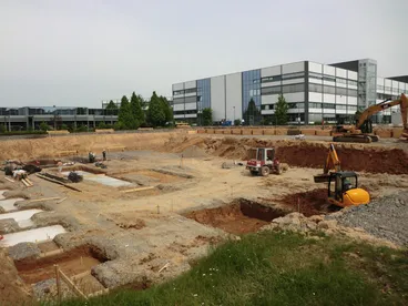 Baugrube mit Fundamentarbeiten vor einem großen Industriegebäude