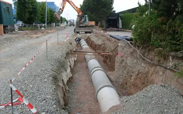 Rohrgraben mit verlegten Betonrohren und Bagger im Hintergrund