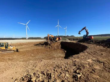 Bagger und Planierraupe bei Erdarbeiten im Windpark, Windräder im Hintergrund
